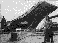Рабочие Черноморского судостроительного завода в Николаеве проходят мимо недостроенного авианесущего крейсера "Варяг" на верфи завода в мае 1997 года